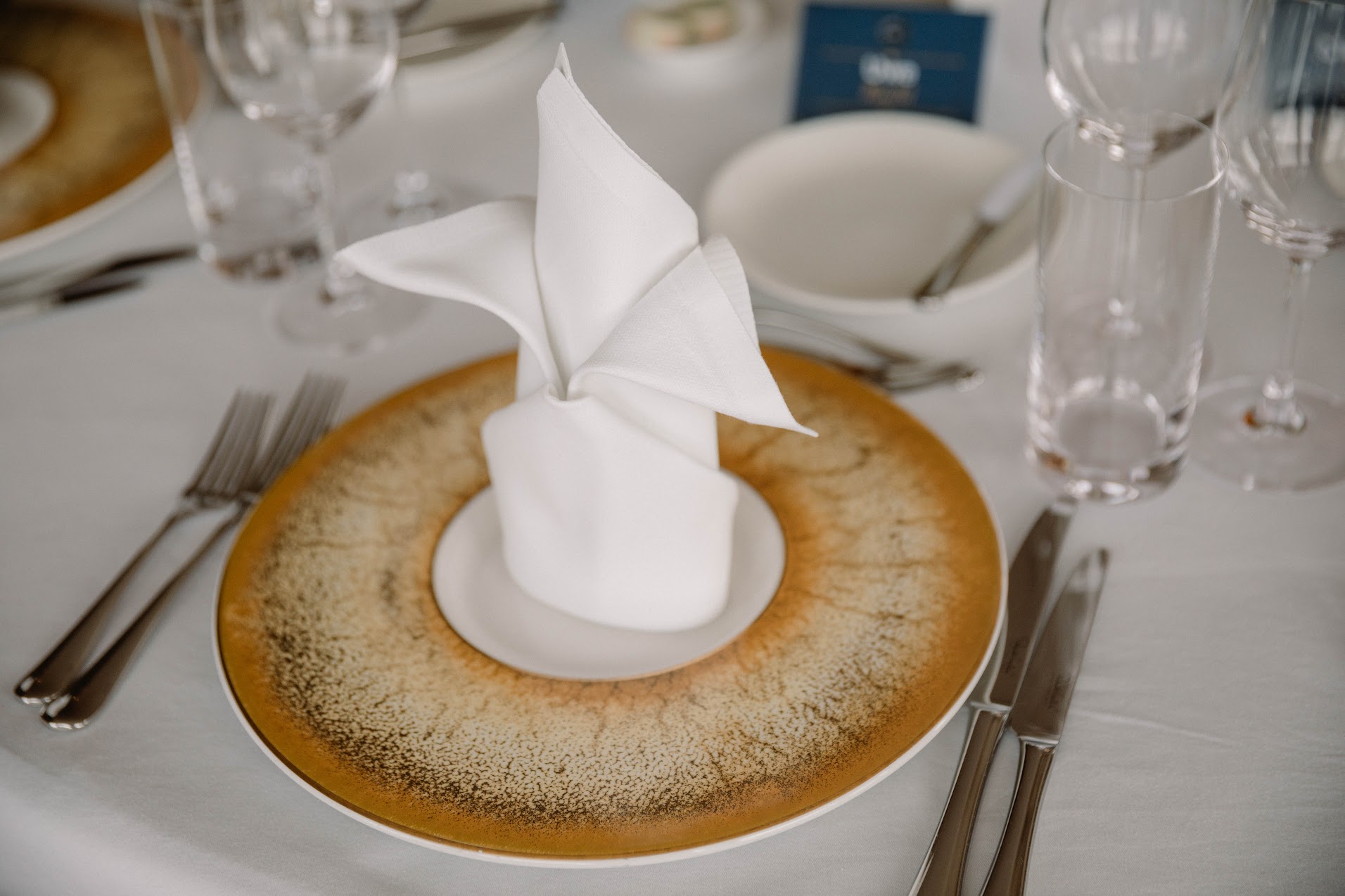 A folded white napkin on a gold charger plate at a formal table
