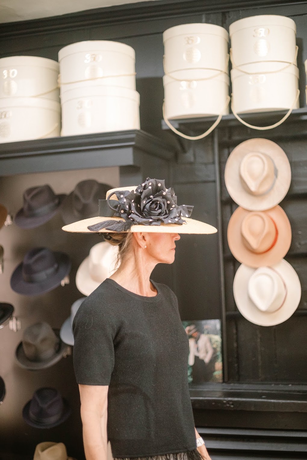 A woman wearing a wide-brimmed hat in a milliner's salon