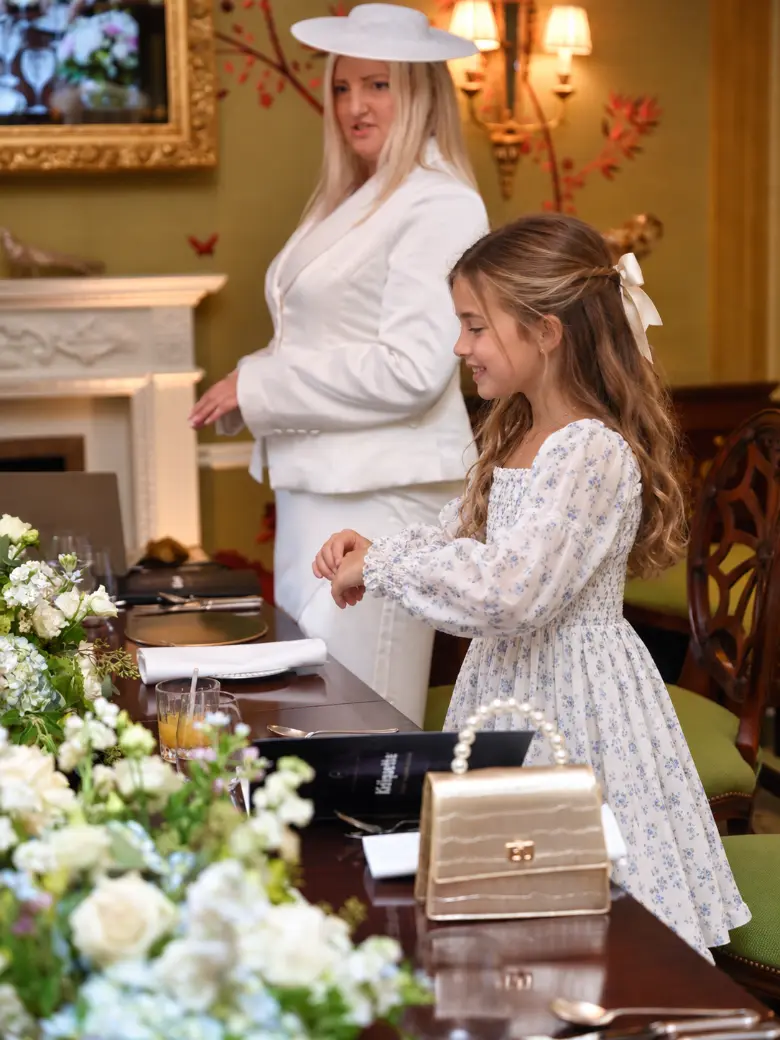 A girl practising table etiquette while her trainer looks on
