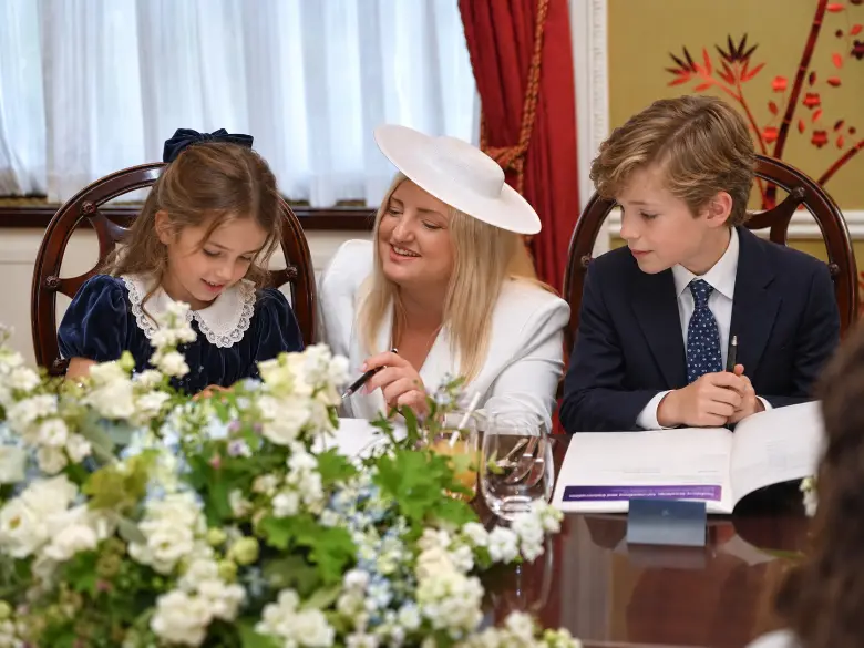 A trainer guiding two children through their workbooks at the table