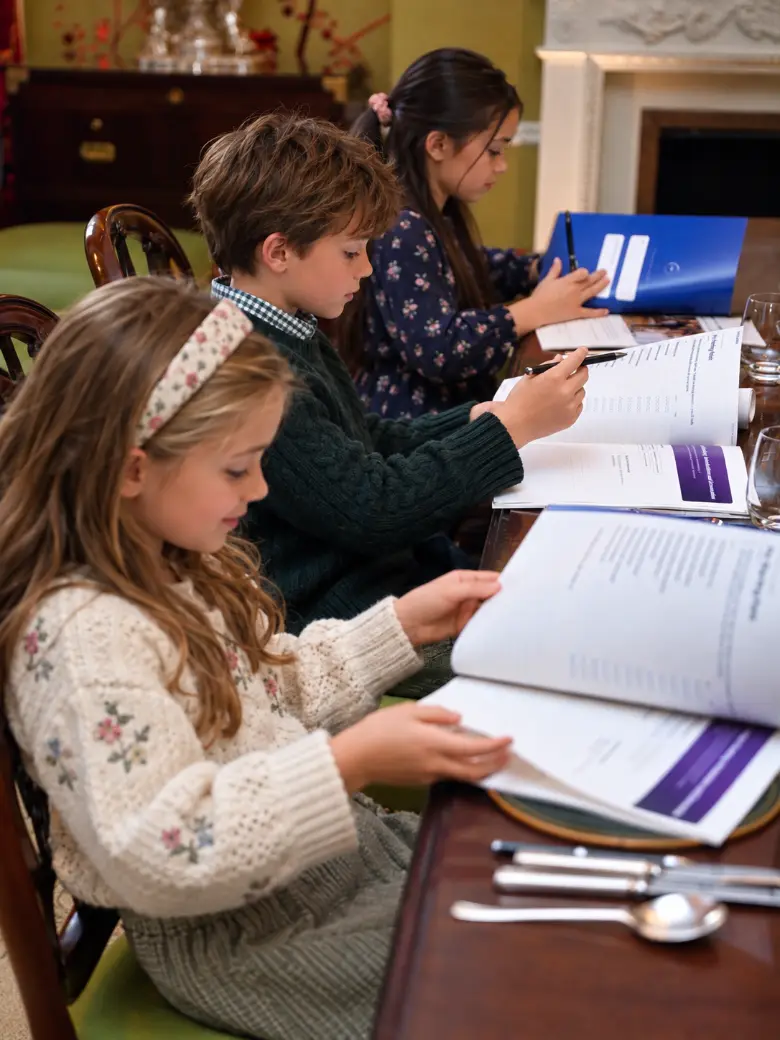 Three children studying their etiquette workbooks at a dining table