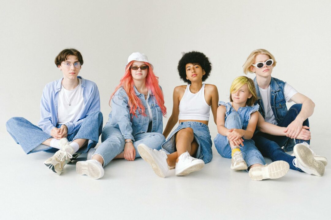 Stylish multiracial teenagers in denim outfits sitting on floor
