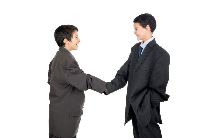 Two boys in smart attire shaking hands while smiling