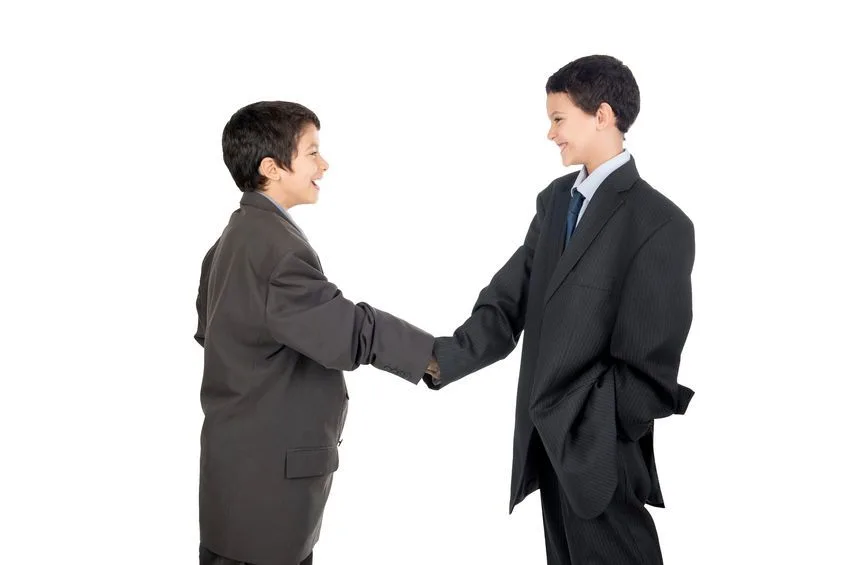 Two boys in smart attire shaking hands while smiling